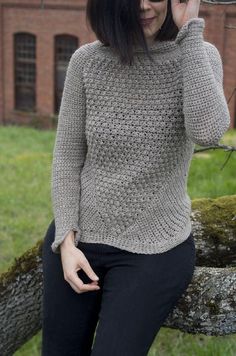 a woman sitting on a tree branch talking on her cell phone while wearing a knitted sweater