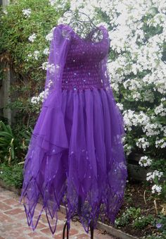 a purple dress sitting on top of a metal stand in front of some white flowers