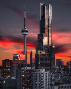 the city skyline is lit up at night with red and blue clouds in the sky