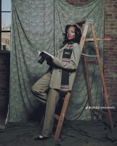 a woman leaning up against a ladder in front of a curtain and holding a book