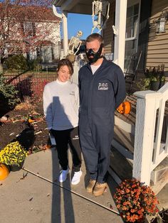 a man and woman standing in front of a house with pumpkins on the porch