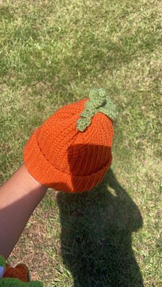 a child's hand wearing an orange knitted hat with a green leaf on it