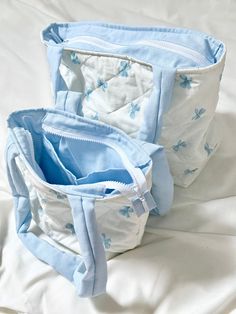 two blue and white bags sitting on top of a bed next to eachother