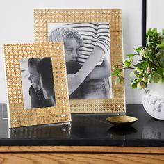 two gold frames sitting on top of a table next to a vase with flowers in it