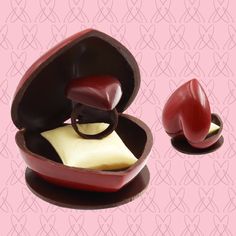 two pieces of chocolate in a red heart shaped box on a pink background with hearts