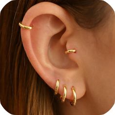 a woman's ear with two gold hoops on top of her ear, and one in the middle