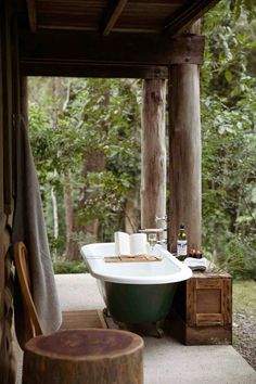 a bath tub sitting under a wooden roof next to a tree stump table and chair