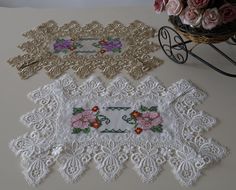 three white doily with flowers on them sitting next to a basket of pink roses