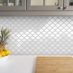 pineapples and lemons sit on a cutting board in front of a white tiled backsplash