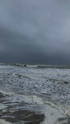 an ocean with waves crashing on the shore and dark clouds in the sky above it