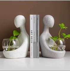 two white sculptures sitting on top of a table next to a book and planter