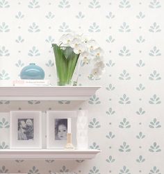 two white shelves with flowers and pictures on them in front of a wallpapered background