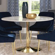 a white table with blue chairs and a gold vase on it in front of a window