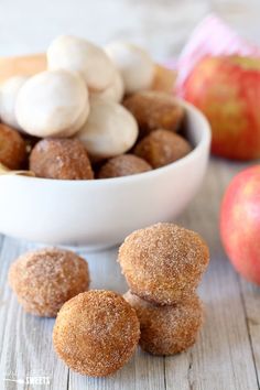 some sugared donuts are in a bowl next to an apple