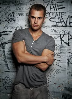 a man standing with his arms crossed in front of a wall covered in grafitti