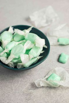 green and white marshmallows are in a bowl on the floor next to some tissue paper