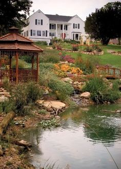 a gazebo sitting in the middle of a garden next to a pond and house