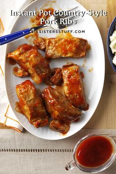 a white plate topped with wings covered in sauce next to a bowl of mashed potatoes