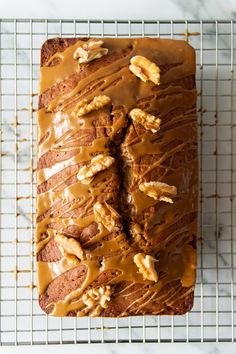 a loaf of banana bread with icing and walnuts on a wire cooling rack