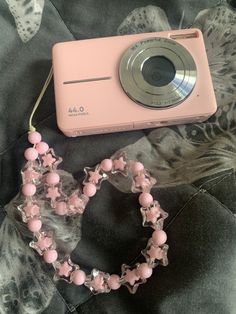 a pink camera sitting on top of a bed next to a beaded bracelet and necklace