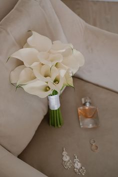 a bouquet of white flowers sitting on top of a couch next to two wedding rings