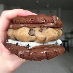 a hand holding a chocolate cookie sandwich with ice cream and chocolate chips on the top