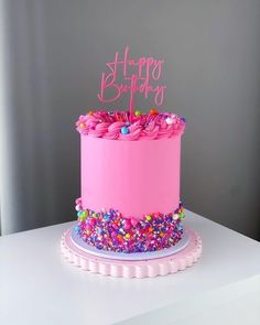 a pink birthday cake with sprinkles and a happy birthday sign on top