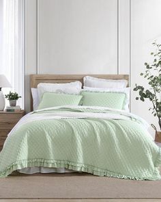 a bed with green comforter and pillows in a white room next to a potted plant