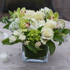 a vase filled with white and green flowers on top of a table next to a candle