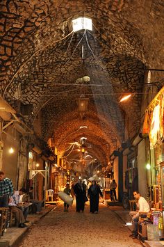 people are walking down an alley way in the middle of a building with stone walls and ceilings