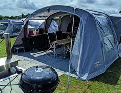 a blue tent is set up in the grass with chairs and grills around it