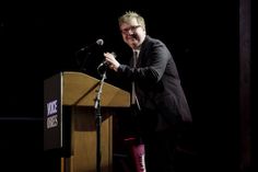 a man standing at a podium with a microphone in front of him and holding his hand out