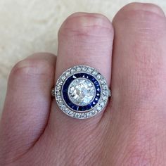 a person's hand holding a ring with a blue and white diamond in it