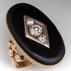 This antique statement ring is centered with one (1) oval cabochon cut natural black onyx. The onyx has been drilled at the center and topped with a white gold navette shaped setting accented with one (1) bead set, old European cut diamond and two (2) bead set, round brilliant cut diamonds. Floral details accent the shoulders of the ring. The ring measures 30.6mm at the top, rises 6.5mm above the finger, tapering to 3.5mm wide and 1.0mm thick at the base of the shank. It is currently a size 10 and is crafted in lightly patinated 14k yellow gold. One of the diamonds has a small unnoticeable chip and the onyx shows light wear. Edwardian Onyx Rings, Luxury Oval Black Enamel Rings, Black Cabochon Signet Ring For Formal Occasions, Formal Black Cabochon Signet Ring, Luxury Oval Signet Ring With Black Enamel, Luxury Oval Black Enamel Signet Ring, Antique Black Rings With Rose Cut Diamonds, Heirloom Black Ring With Cabochon, Antique Oval Onyx Jewelry