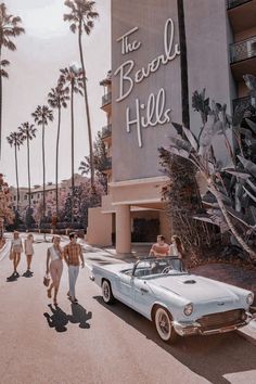 two people walking down the street in front of a hotel with cars and palm trees