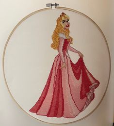 a cross stitched picture of a princess in a pink dress on a white wall