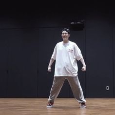 a man standing on top of a wooden floor in front of a black wall and wearing white t - shirt