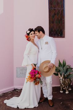 a bride and groom standing in front of a pink wall