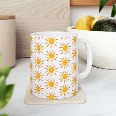 an orange and white mug sitting on top of a counter next to some fruit in a bowl