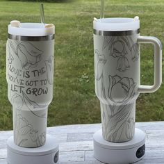 two coffee mugs sitting next to each other on top of a wooden table in the grass