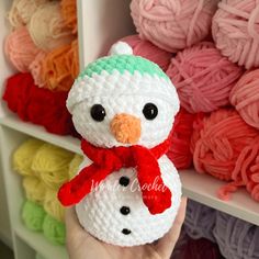 a crocheted snowman with a red scarf on it's head in front of yarn balls