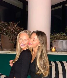 two beautiful young women sitting next to each other on top of a black and white couch