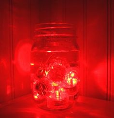 a jar filled with candles sitting on top of a table next to a red light