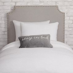 a bed with white sheets and pillows on top of it next to a brick wall