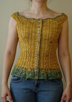 a woman wearing jeans and a yellow top with buttons on it's shoulders, standing in front of a white wall