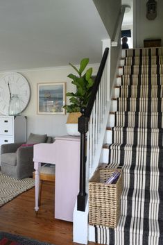 a living room filled with furniture and a stair case next to a clock on the wall