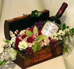 a bottle of wine sitting on top of a wooden box filled with flowers and berries