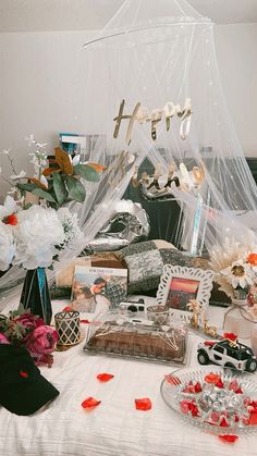 a bed covered in white sheets and flowers next to a table topped with cakes, candies and other items