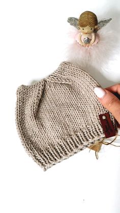 a hand holding a knitted mitt next to a small angel figurine