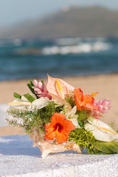 a bouquet of flowers sitting on top of a table next to the ocean with waves in the background